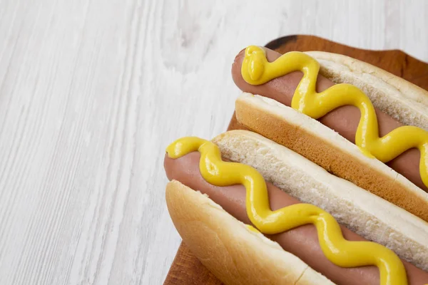 To hotdogs med gul sennep på en rustik træplade på en - Stock-foto