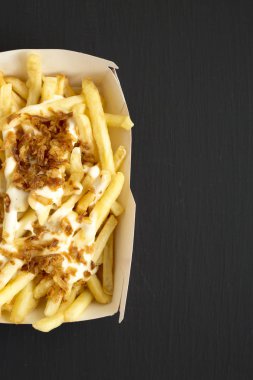 Bir bla üzerinde bir kağıt kutusunda peynir sosu ve soğan ile patates kızartması