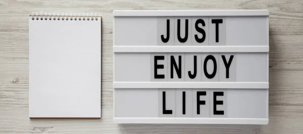 「人生を楽しむだけ」の言葉を持つライトボックス、ホイット上の空白のメモ帳 — ストック写真