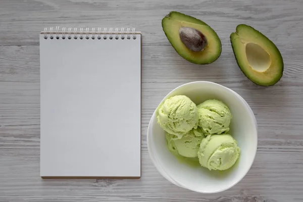 Homemade avocado ice cream in a bowl, blank notebook over white
