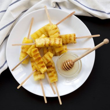 Siyah bir yüzeyde beyaz bir plakada ızgara ananas dilimleri,