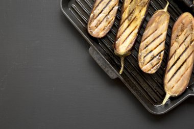 Siyah bir yüzeyde bir ızgara tava üzerinde patlıcan, üst görünüm. Düz La