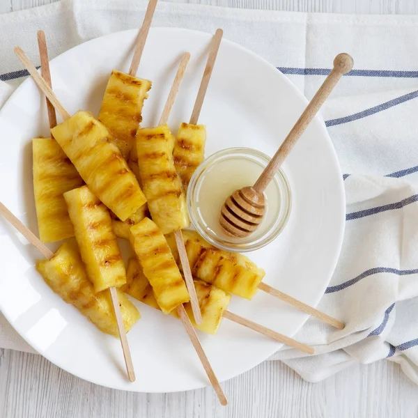 Grilled pineapple on bamboo sticks with honey on a white plate,