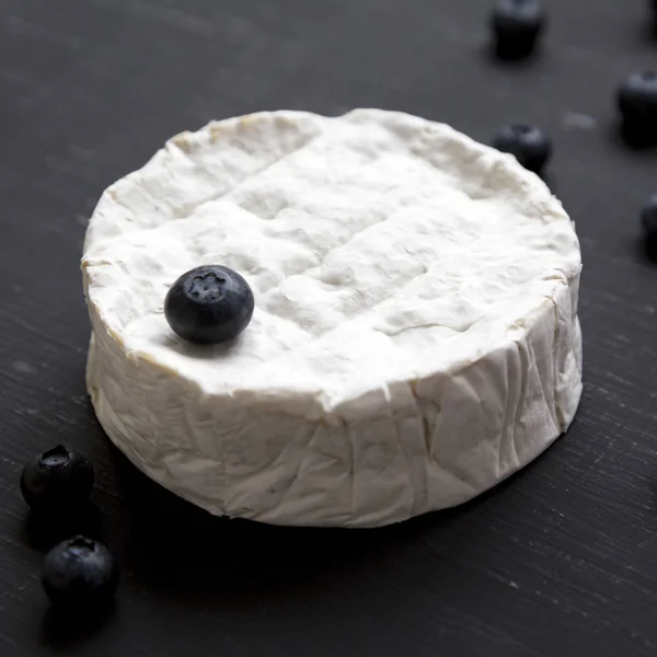 Camembert cheese with blueberries on a black background, side vi — Stock Photo, Image