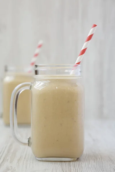 Batido de plátano con mantequilla de maní en frascos de vidrio sobre una ba de madera blanca —  Fotos de Stock