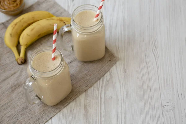 Peanut butter banana smoothie in glass jars on a white wooden ba