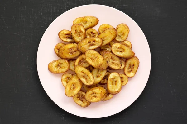 Plantains frits faits maison sur une assiette rose sur un fond noir , — Photo