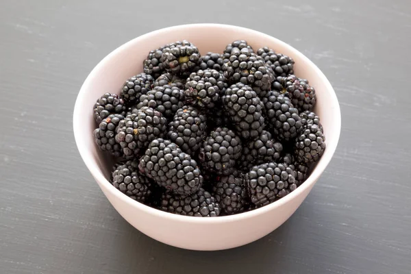 Blackberries in a pink bowl over black background, side view. Su