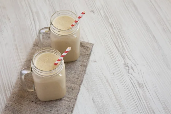 Tazas de tarro de vidrio llenas de mantequilla de maní batido de plátano en un wh — Foto de Stock