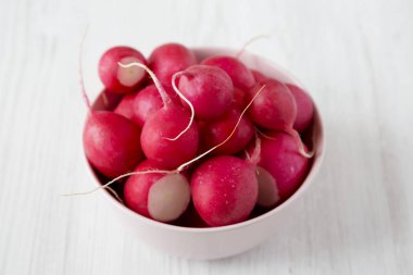 Beyaz ahşap yüzeyüzerinde pembe bir kapta taze turp, yan vi