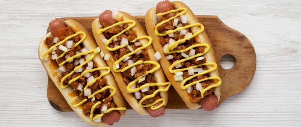 Homemade detroit style chili dog on a rustic wooden board on a w