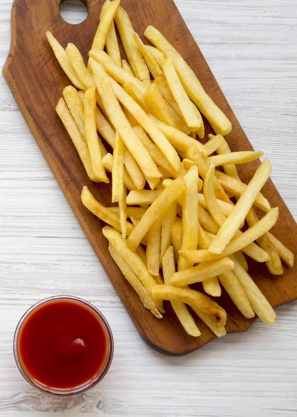 Papas fritas en una tabla rústica de madera y ketchup en un coro blanco — Foto de Stock