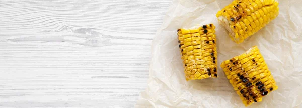 Grilled corn on the cob on a white wooden background, top view.