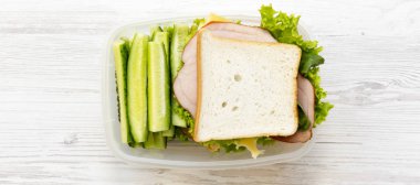 Beyaz ahşap yüzeyüzerinde sandviç ve sebze ile Öğle yemeği kutusu