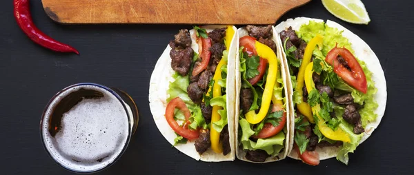 Tacos con carne y verduras, cerveza y lima sobre una superficie negra — Foto de Stock