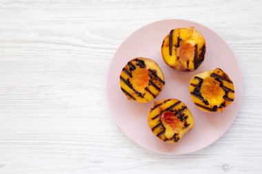 Beyaz ahşap bir sırt üzerinde pembe bir tabak üzerinde ev yapımı ızgara şeftali