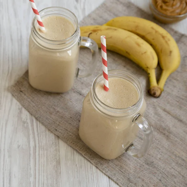 Peanut butter banana smoothie in glass jars on a white wooden ta