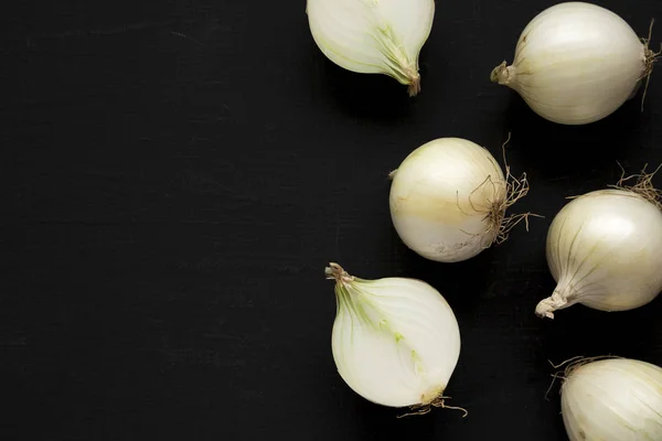 Raw white onions on a black surface, top view. Flat lay, overhea