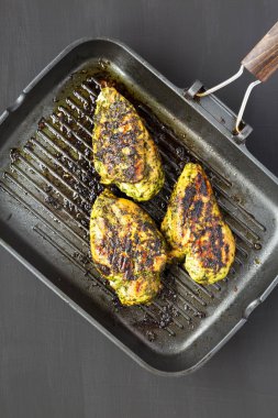 Grilled chimichurri chicken breast in a grilling pan on a black  clipart