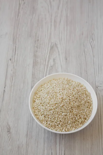 Organic Arborio rice in a white bowl on a white wooden backgroun — Stock Photo, Image
