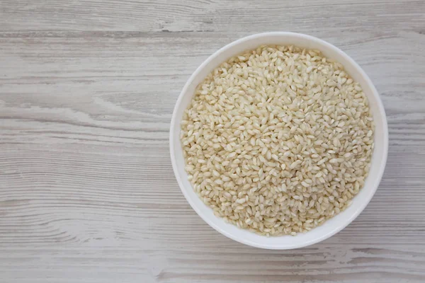 Organic Arborio rice in a white bowl on a white wooden backgroun — Stock Photo, Image