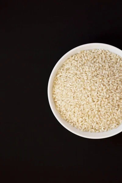 Organic Arborio rice in a white bowl on a black surface, top vie — Stock Photo, Image