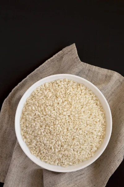 Organic Arborio rice in a white bowl on a black surface, top vie — Stock Photo, Image