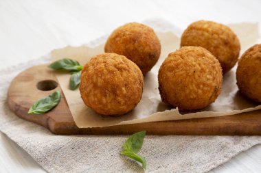 Beyaz ahşap arka plan üzerinde fesleğen ile ev yapımı kızarmış Arancini,