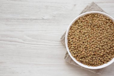 Beyaz ahşap yüzey üzerinde beyaz bir kapta organik yeşil mercimek,