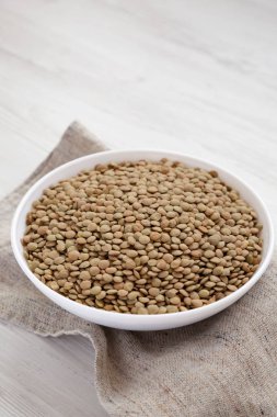 Beyaz ahşap yüzey üzerinde beyaz bir kapta organik yeşil mercimek,