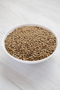 Beyaz ahşap yüzey üzerinde beyaz bir kapta organik yeşil mercimek,