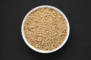 Siyah bir yüzey üzerinde beyaz bir kapta Organik yeşil mercimek, üst vi