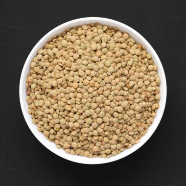 Siyah bir arka plan üzerinde beyaz bir kapta Organik yeşil mercimek, üst