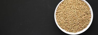 Organik yeşil mercimek siyah bir yüzey üzerinde beyaz bir kapta, overhe