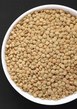 Siyah bir yüzey üzerinde beyaz bir kapta Organik yeşil mercimek, üst vi