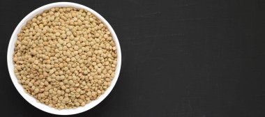 Siyah bir arka plan üzerinde beyaz bir kapta Organik yeşil mercimek, vie