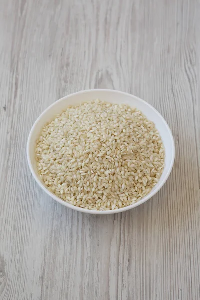 Organic Arborio rice in a white bowl on a white wooden surface, — Stock Photo, Image