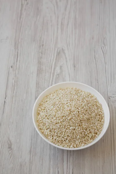 Riz Arborio bio dans un bol blanc sur un fond de bois blanc — Photo