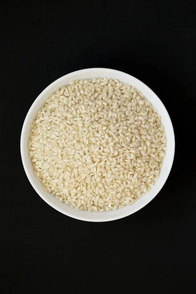 Organic Arborio rice in a white bowl on a black background, top — Stock Photo, Image