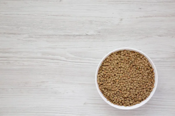 Beyaz ahşap yüzey üzerinde beyaz bir kapta organik yeşil mercimek,