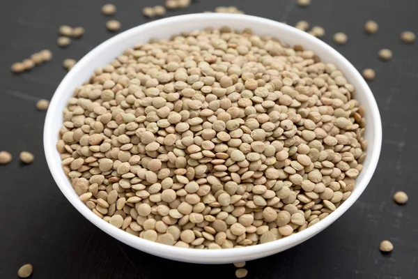 Organik yeşil mercimek siyah bir yüzeyüzerinde beyaz bir kapta, yan v