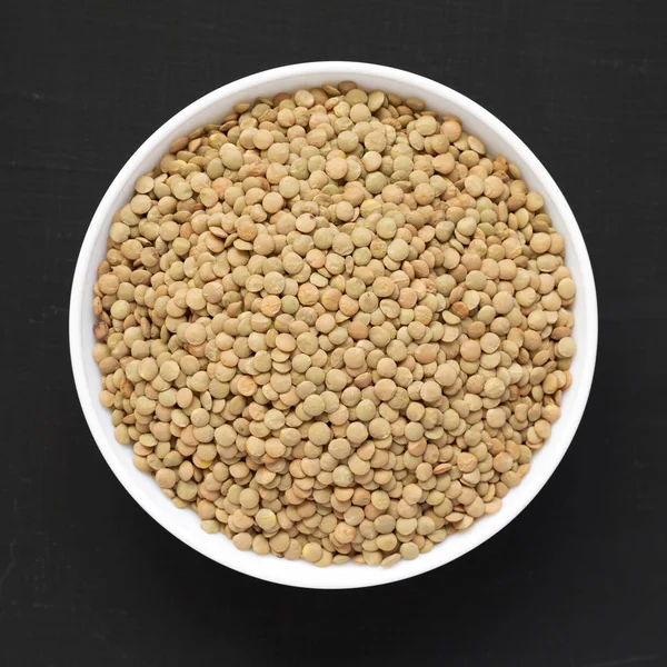 Siyah bir arka plan üzerinde beyaz bir kapta Organik yeşil mercimek, üst