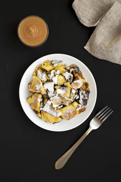 Ev yapımı Alman Kaiserschmarrn gözleme siyah bir yüzey üzerinde beyaz bir tabak üzerinde, üst görünümü. Düz yatıyordu, yukarıdan, yukarıdan. 