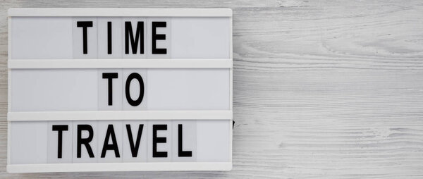 'Time to travel' words on a modern board on a white wooden background, top view. Overhead, from above, flat lay. Copy space.