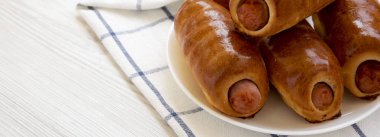 Beyaz bir ahşap üzerinde beyaz bir tabak üzerinde ev yapımı sığır sosis kolache