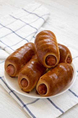 Beyaz bir ahşap üzerinde beyaz bir tabak üzerinde ev yapımı sığır sosis kolache