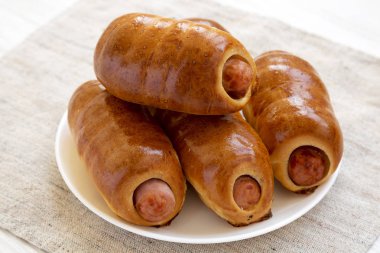 Beyaz bir ahşap üzerinde beyaz bir tabak üzerinde ev yapımı sığır sosis kolache
