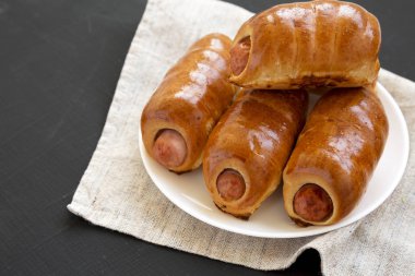 Siyah bir backgr üzerinde beyaz bir tabak üzerinde ev yapımı sığır sosis kolache