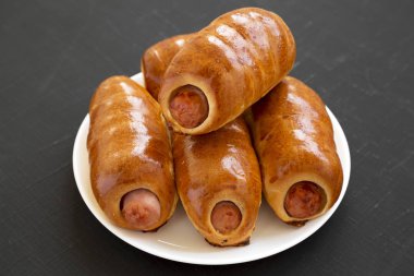 Siyah bir surfac üzerinde beyaz bir tabak üzerinde ev yapımı sığır sosis kolache