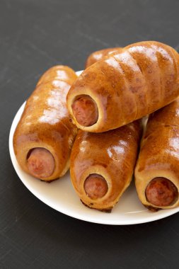 Siyah bir surfac üzerinde beyaz bir tabak üzerinde ev yapımı sığır sosis kolache